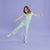 A young girl with light brown hair is posing in a mint green short-sleeve jumpsuit with small white polka dots, paired with matching mint sneakers, against a solid lavender studio backdrop.