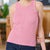 A woman wearing a pink ribbed tank top and dark blue jeans, standing in a softly blurred indoor setting.
