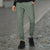 A person wearing heathered sage green jogger pants and black sneakers walking on a cobblestone street.