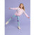A young girl with curly blonde hair is captured mid-motion in a playful pose, wearing a pastel pink and lavender knit cardigan, light blue jeans with purple heart patches, and white sneakers, set against a solid lavender studio background.