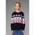A young boy wearing a navy blue Christmas sweater with white and red holiday patterns, paired with blue jeans, standing against a solid gray background.