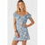 A woman modeling a light blue off-the-shoulder floral mini dress with puff sleeves and a button-down front, set against a plain light gray studio background.