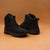 A pair of black high-top athletic sneakers shown from the side and back on a warm, solid brown studio background.