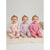 Three smiling babies sitting side by side on a cream textured blanket, wearing matching long-sleeve pajamas in pink, lavender, and peach tones with floral and butterfly patterns.