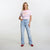 A woman modeling a light pink graphic t-shirt with red trim and light-wash blue jeans, standing against a plain white studio background.