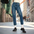 A person wearing blue straight-leg jeans, white socks, and black leather shoes standing on a city street.