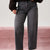 A person wearing dark gray wide-leg jeans and a dark brown fuzzy cropped sweater, standing against a split white and dusty pink background.