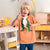 A young blonde boy wearing a short-sleeve orange t-shirt with a green dinosaur graphic, posing in a brightly lit children's room.