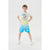 A young boy modeling a two-piece outfit consisting of a light yellow t-shirt with a cartoon graphic and the words 'THE GOOD LIFE' and matching light blue gradient shorts with Snoopy graphics, set against a plain light gray studio background.
