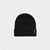 A black ribbed knit beanie hat with a folded cuff, featuring a small black brand patch on the side, set against a plain light gray background.