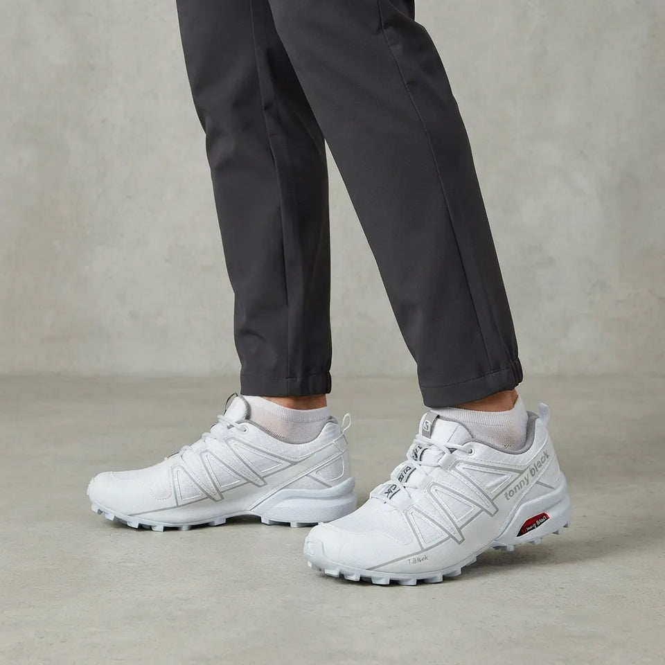 White Salomon Speedcross trail running shoes worn with dark gray pants and white socks, shown from the knees down on a textured concrete floor.