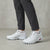 White Salomon Speedcross trail running shoes worn with dark gray pants and white socks, shown from the knees down on a textured concrete floor.