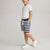 A child model wearing a white t-shirt, navy and white striped shorts, and white sneakers, standing against a light gray studio background.