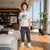 A smiling boy stands in a modern living room wearing a light gray graphic t-shirt with a yellow and blue 'ARE YOU READY? TRAILER FIGHT!' print, dark gray jogger pants, and white sneakers with green accents.