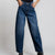 A person wearing dark blue wide-leg denim jeans with a straight-to-relaxed leg, paired with a black top and black boots, shown from the waist down against a light gray studio background.