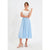 A woman modeling a light blue pleated midi skirt paired with a cream short-sleeve top and clear heeled sandals, standing against a plain white studio background.