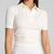A woman wearing a fitted short-sleeve polo shirt in off-white/cream, shown from the neck to the hips against a light gray studio background.