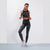A woman modeling a matching black and gray marbled activewear set, featuring a high-neck crop top and high-waisted leggings, paired with white sneakers, against a light gray studio background.
