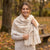 A woman smiling in an autumn park, wearing a large cream-colored plaid shawl over a light beige sweater.