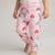 A child wearing light pink jogger-style pants with a pattern of pink, magenta, and lavender-blue hearts, paired with a white top, shown from the waist down against a light gray studio background.