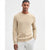 A man wearing a beige textured knit crewneck sweater and white trousers, standing against a plain light gray studio background.
