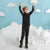 A young boy wearing a black full-body snowsuit with small white speckles and lime green accents stands in a snowy play area with a light blue wall decorated with white clouds.