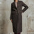 A woman wearing a dark brown textured wool-blend coat over a ribbed knit top, standing against a distressed concrete wall.