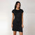 A woman modeling a short-sleeve black textured dress with a crew neck and side ruching, standing against a plain light gray studio background.