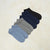 Six pairs of low-cut ankle socks arranged in a fan shape on a textured beige background. The socks come in six different colors: light blue, heather gray, navy blue, and black.