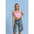 A model wearing a light pink scoop-neck crop top and light-wash blue denim cargo shorts with a black belt, standing against a solid light blue background.