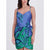 A woman wearing a sleeveless wrap-style mini dress with thin straps, a blue bodice, and a green tropical leaf print, photographed against a light gray studio background.