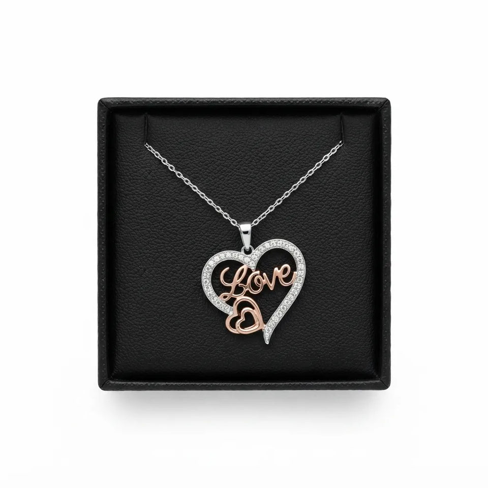 A silver and rose gold heart pendant necklace with the word 'Love' written in script, displayed on a black textured gift box against a white background.