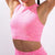 A close-up of a model wearing a bright pink athletic crop top with a subtle tonal textured pattern, paired with matching pink bottoms against a light gray background.