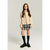 A young girl stands against a light gray studio background wearing a beige double-breasted jacket, a black and white plaid mini skirt, black knee-high socks, and black leather shoes.
