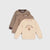 Three children's long-sleeve tops arranged in a stack on a light gray background: a cream sweatshirt with a teddy bear graphic and 'MASTER OF MUGS' text, a taupe sweatshirt, and a brown-and-beige striped top.