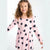 A young girl with curly brown hair wearing a light pink long-sleeve dress with a black heart pattern, photographed against a plain white studio background.