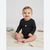 A baby sitting on a cream knit blanket wearing a black long-sleeve bodysuit with a ruffled collar and a small white heart on the chest.