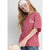 A young girl with long blonde hair wearing a dusty rose pink t-shirt with a white 'KIND HEART' graphic on the left chest, paired with a white headband and blue jeans, holding a beige bag against a light gray background.