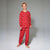 A young boy stands barefoot against a light gray studio background, wearing a red long-sleeve pajama set with a repeating gold floral pattern.