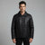 A man wearing a black leather jacket with a zippered front and collar, standing against a solid gray studio background.