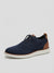 A navy blue knit lace-up sneaker with brown leather accents on the heel and toe, featuring a thick white sole, shown against a light gray background.