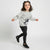 A young girl smiling and posing in a light gray sweatshirt with a dog graphic and the text 'pet a dog', paired with black leggings featuring small pink hearts and black sneakers, set against a plain light gray studio background.