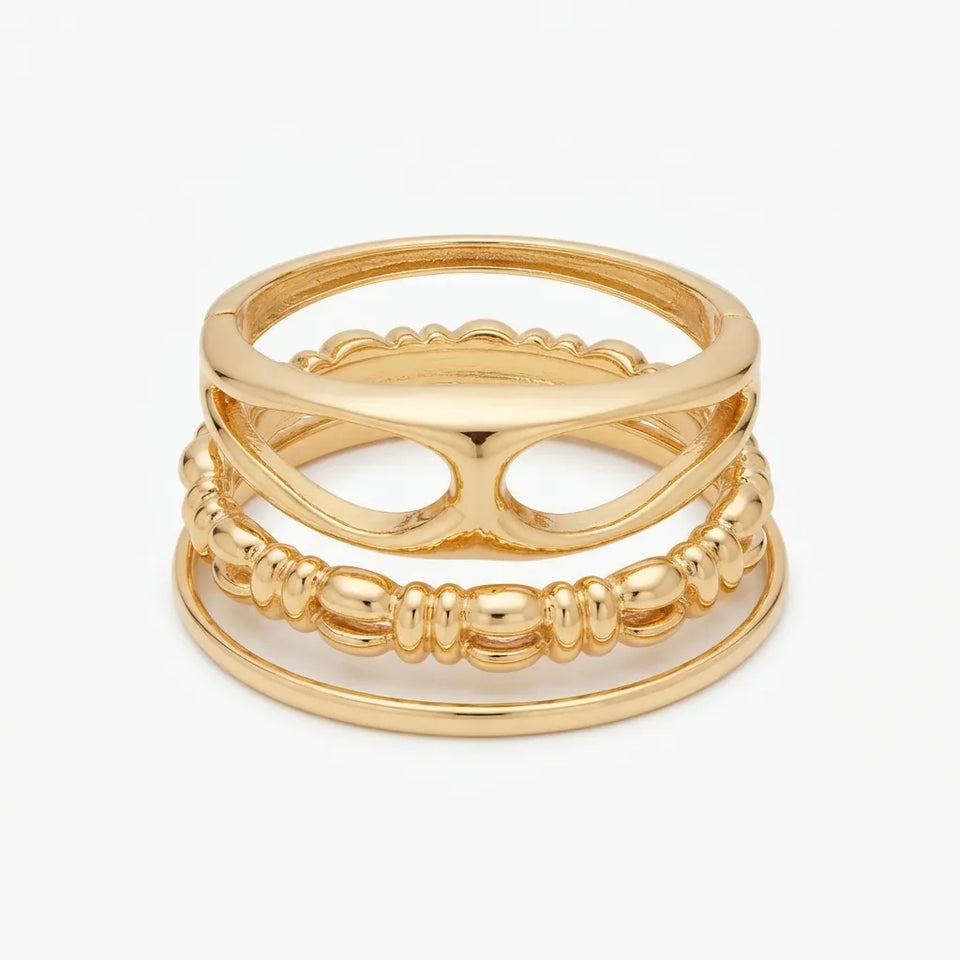 A stack of three gold rings with unique designs, including a scalloped band, a beaded textured band, and a smooth thin band, displayed on a light gray background.