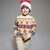 A young boy wearing a festive Christmas sweater and Santa hat, standing against a neutral gray studio background.