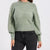 A woman wearing a light sage green knit sweater with balloon sleeves and dark gray jeans, shown from the neck down against a plain white background.