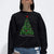 A woman wearing a black crewneck sweatshirt with a green Christmas tree graphic and 'Merry Christmas' text, paired with distressed blue jeans against a plain white background.