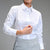 A woman wearing a crisp white long-sleeve button-down shirt tucked into a light gray skirt, shown from the chin down against a solid gray studio background.
