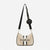 Bebe brand shoulder bag in beige textured canvas with black leather trim, black vertical stripes, a black adjustable shoulder strap, a gold chain detail, and a small black circular coin pouch with the brand name.
