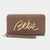 A brown leather zip-around wallet with a wristlet strap and a large gold metallic 'Bebe' script logo on the front, set against a plain light gray background.