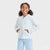 Young girl wearing a light gray hoodie and light blue jeans on a white background